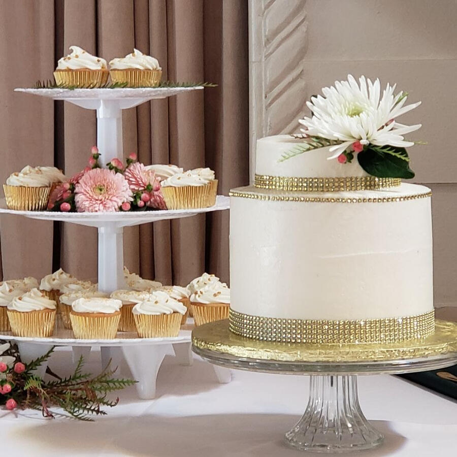 Dessert table with a tiered cupcake stand and a white cake topped with a flower