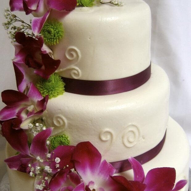 Three-tier ivory wedding cake with cascading magenta orchids and burgundy ribbon