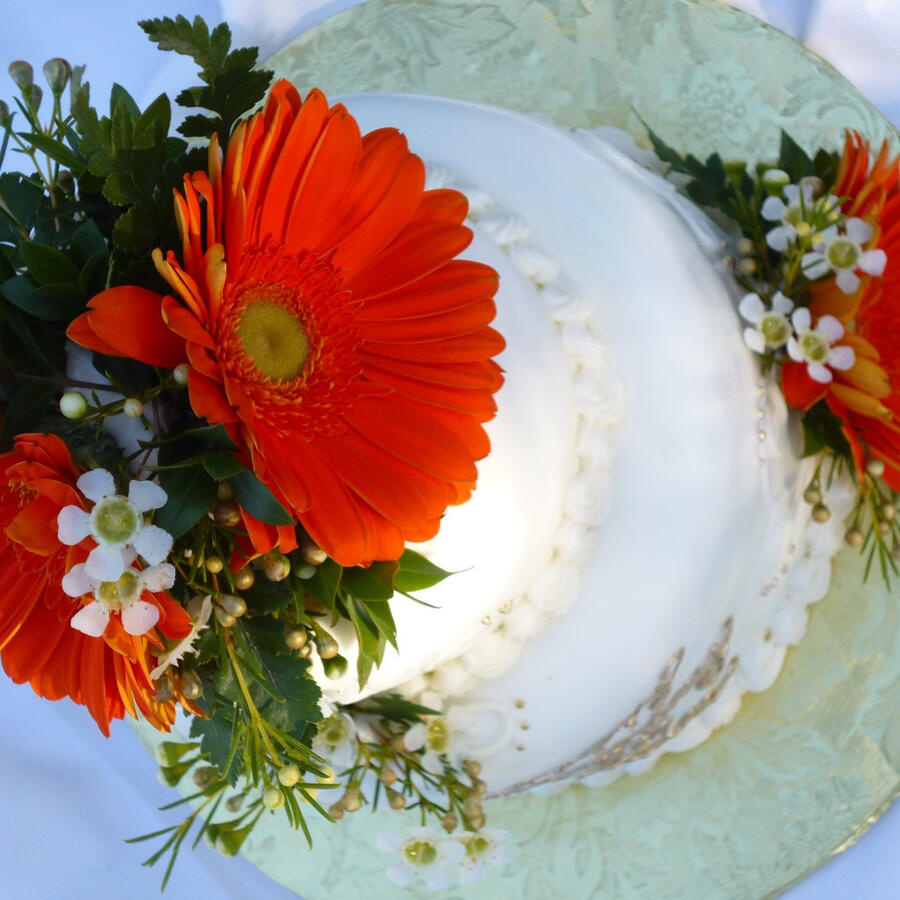 White cake topped with bright orange gerbera daisies and baby's breath White cake topped with bright orange gerbera daisies and baby's breath