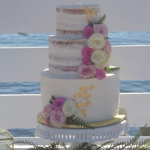 Four-tier white wedding cake with cascading pink roses on a silver cake stand