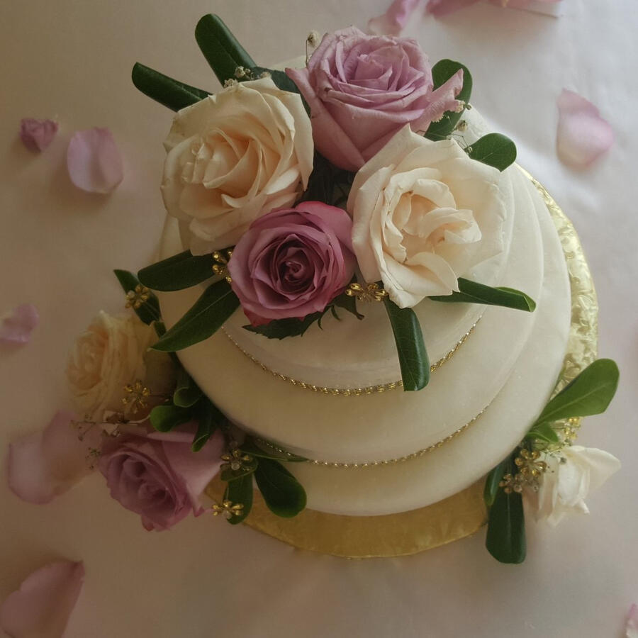 Round white cake topped with pink and lavender roses, petals scattered around it