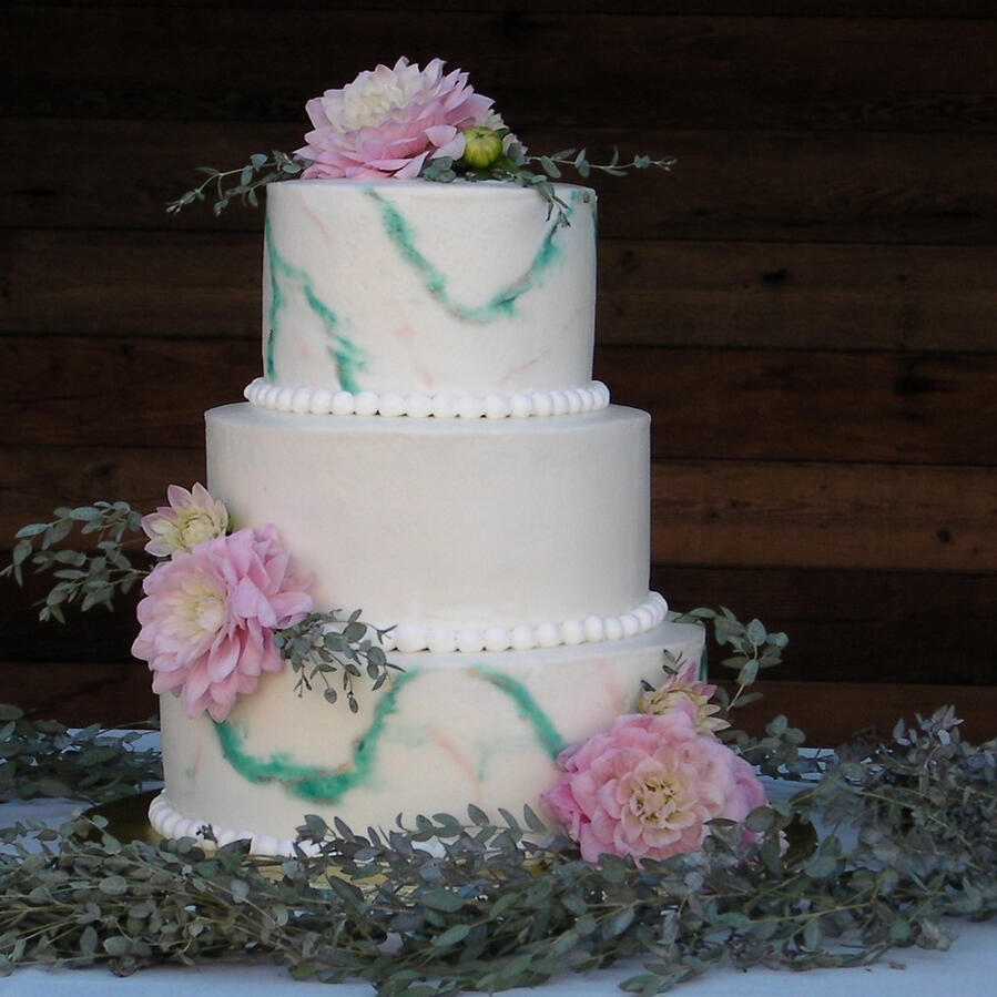 Three-tier white wedding cake with pink and lavender flowers on a reception table