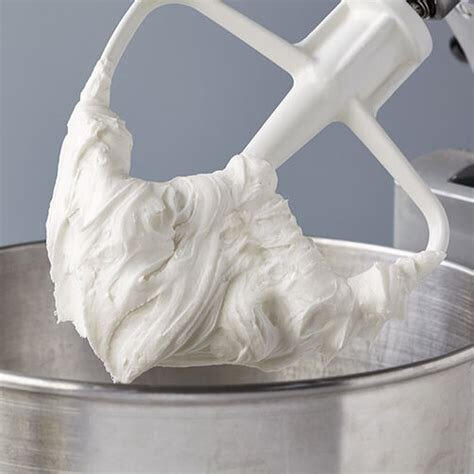 Stand mixer whisk coated in fluffy white buttercream